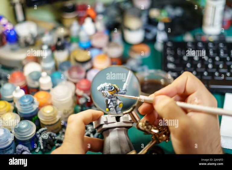 man-painting-miniatures-of-board-game-with-large-magnifying-glass-2JAHJFD